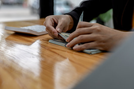 Woman counting dollar bills, she is a cashier serving customers in front of the cashier counter, she...