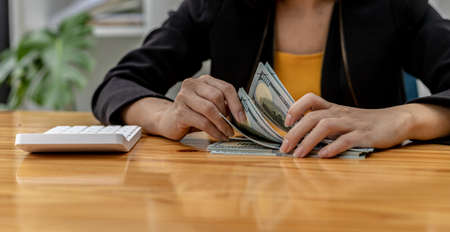 Woman counting dollar bills, she is a cashier serving customers in front of the cashier counter, she counts the money after the service is closed to verify the balance. Conceptual image of money.の写真素材