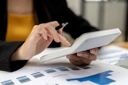 The company's finance manager is using a calculator, he uses a calculator to calculate the numbers in the company's financial documents that employees in the department create as meeting documents.の写真素材