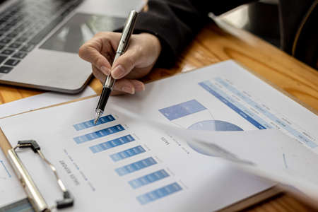 Businesswoman's hand holding a pen pointing at a bar chart on a corporate financial information sheet, the businesswoman examines the financial information provided by the finance department.の写真素材