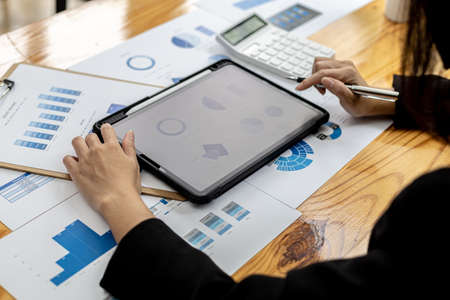 A businesswoman holding a tablet that opens the company's financial documents from the finance department, she checks the information in the documents to analyze the financial management plan.の写真素材