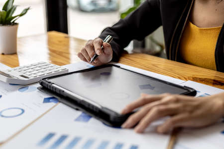 A businesswoman holding a tablet that opens the company's financial documents from the finance department, she checks the information in the documents to analyze the financial management plan.の写真素材