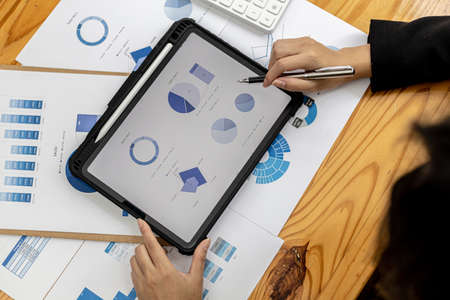 A businesswoman holding a tablet that opens the company's financial documents from the finance department, she checks the information in the documents to analyze the financial management plan.の写真素材