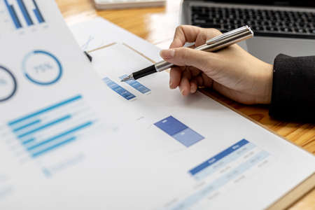 Businesswoman's hand holding a pen pointing at a bar chart on a corporate financial information sheet, the businesswoman examines the financial information provided by the finance department.の写真素材