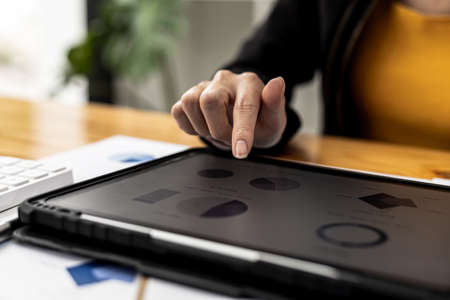 A businesswoman holding a tablet that opens the company's financial documents from the finance department, she checks the information in the documents to analyze the financial management plan.の写真素材