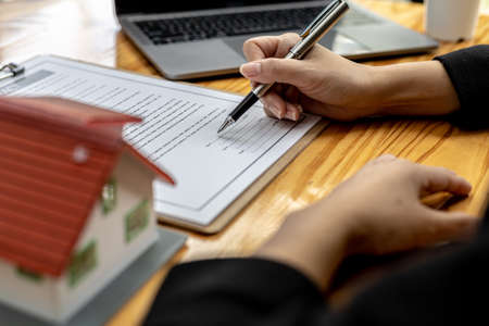 Real estate contract agreement concept. Buyer is signing house purchase contract with seller. Salesperson calculates house purchase cost and explains details on contract.の写真素材