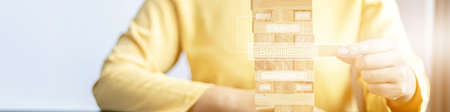 A woman plays a game of wooden blocks that are building blocks, she is picking up a block of wood from a row, like managing a business on risk, management to make the business grow and be profitable.の写真素材