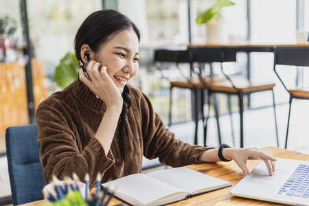An Asian female student using a laptop, she is studying online, she looks at the laptop intently listening to what the teacher is teaching. Online learning concept.の写真素材