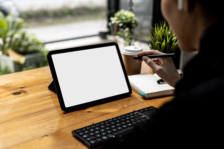 A woman holding a pen pointing to a with a white blank screen, on a white background tablet screen for inserting text or advertising graphics. The concept of using technology. copy space.の写真素材