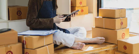 Business owner opens an online store, she is checking orders from customers via a tablet, sending goods through a courier company, the concept of a woman opening an online business.の写真素材