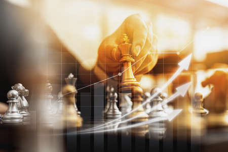 Person holding golden chess pieces to run a game, conceptual image of businessman playing chessboard compared to managing a business on risk, chart graphics showing financial flows.の写真素材