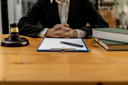 A lawyer sits in his office, on a table with a small hammer to beat the judges desk in court. and justice scales, lawyers are drafting a contract for the client to use with the defendant to sign.の写真素材