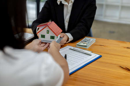 Two people holding a small model house, the home salesman handing over the house to the customer...