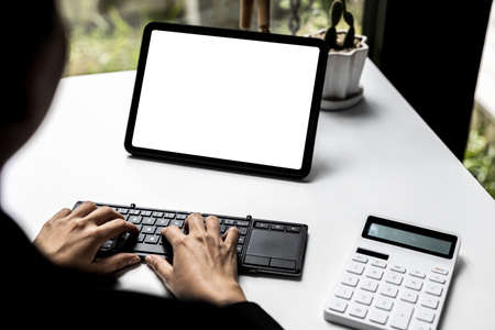 Tablet blank screen, person looking at blank tablet screen and typing on keyboard, screen mockup for further editing can be used for a variety of tasks. copy space.の写真素材