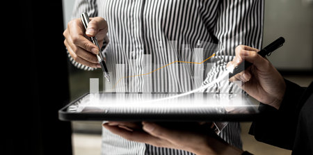 Two business people using a tablet to view company financial reports, graphics showing financial and numerical growth data. The concept of financial management to grow and be profitable.の写真素材