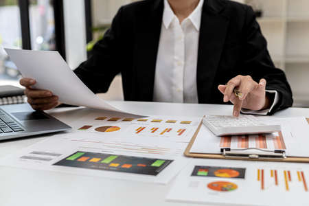 The company's finance manager is using a calculator, he uses a calculator to calculate the numbers in the company's financial documents that employees in the department create as meeting documents.の写真素材