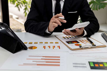The company's finance manager is using a calculator, he uses a calculator to calculate the numbers in the company's financial documents that employees in the department create as meeting documents.の写真素材