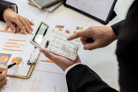Two people checking numbers on documents using calculators, business people brainstorming ideas to solve losses and planning strategies to keep the company profitable and growing.の写真素材