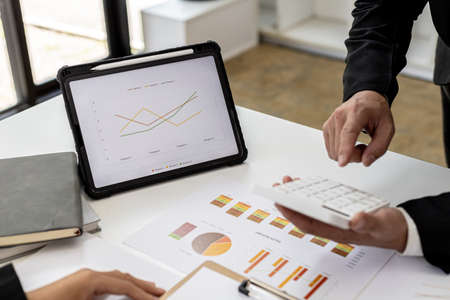 Two people checking numbers on documents using calculators, business people brainstorming ideas to solve losses and planning strategies to keep the company profitable and growing.の写真素材