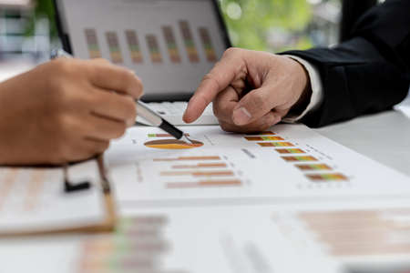 Two people pointing to a company financial summary, two businessmen brainstorming ideas to resolve losses and planning strategies to keep the company profitable and growing.の写真素材