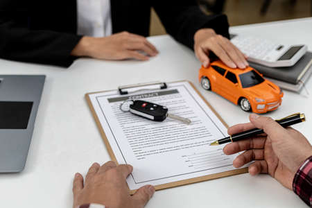 The renter is signing a car rental agreement with the car rental company. After discussing the details and charges with the employee, the employee hand over the car keys to the renter.の写真素材