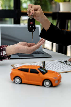 A car rental company employee is handing out the car keys to the renter after discussing the rental details and conditions together with the renter signing a car rental agreement. Concept car rental.の写真素材
