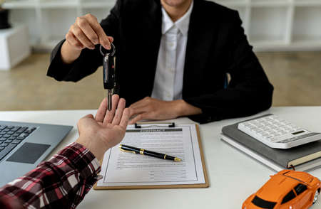 A car rental company employee is handing out the car keys to the renter after discussing the rental details and conditions together with the renter signing a car rental agreement. Concept car rental.の写真素材