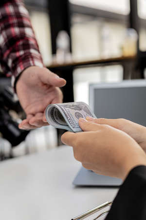 Two people are handing each other dollar bills, they are mutually beneficial business partners, they commit bribery fraud for business interests. The concept of corruption and bribery.の写真素材