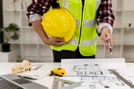 The architect-engineer stood holding a hat and pointed a pen to the floor plan of the house on the table, he was reviewing the work he had designed before presenting it to the client. Interior Design.の写真素材