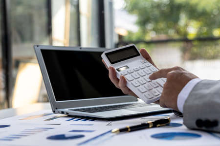 Businessman using a calculator to calculate numbers on a company's financial documents, he is analyzing historical financial data to plan how to grow the company. Financial concept.の写真素材