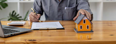 Salesman holding an orange model of a small house, a housing project salesman is drafting a sales contract for a customer who reserves a house in a project he maintains. Real estate trading concept.の写真素材