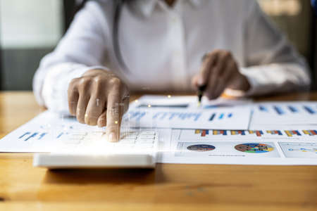 Businesswoman presses a calculator to check data on documents, company financial reports, graphics showing financial and numerical growth data. Financial management to grow and be a profitable conceptの写真素材