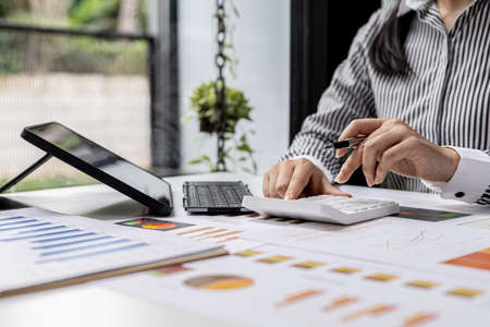 The company's finance manager is using a calculator, he uses a calculator to calculate the numbers in the company's financial documents that employees in the department create as meeting documents.の写真素材