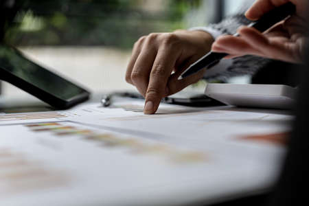 Close-up photo of two businessmen pointing at a sales data sheet in graph format, they are meeting...