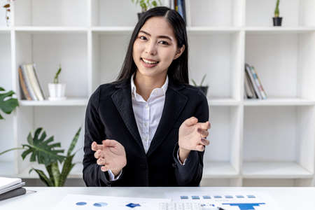 Portrait of a beautiful Asian woman posing talking to the camera. Young business women are raising both hands as if they are video calling with a person. Visual concept for video conferencing.の写真素材