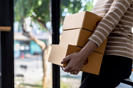 Beautiful Asian woman lifting a bunch of parcels, she owns an online store, she packs and ships through a private transport company. Online selling and online shopping concepts.の写真素材