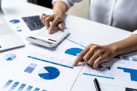 Businesswoman using a white calculator, a financial businessman examining the numerical data on a company financial document, she uses a calculator to verify the accuracy of numbers.の写真素材