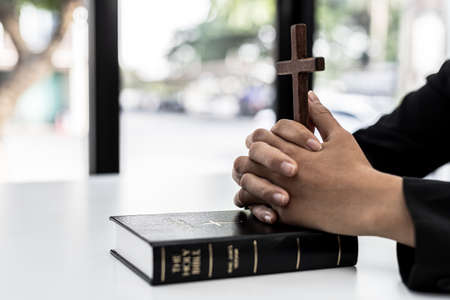A person interlacing his hands on the book of the Bible and holding a cross, he is praying to the Bible, he reads and studies the Bible. Concept of Christianity and Bible Study.の写真素材