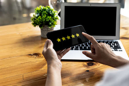 Person holding a smartphone with a screen showing 5 yellow stars, is reviewing a product through an...