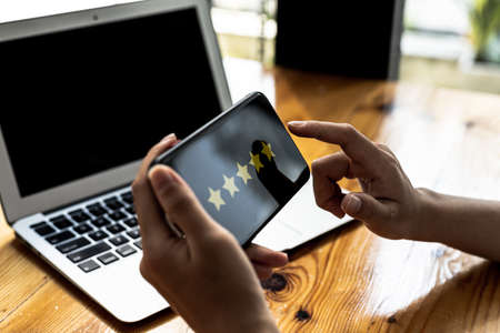 Person holding a smartphone with a screen showing 5 yellow stars, is reviewing a product through an...