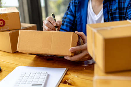 Asian person writing customer's shipping information on parcel box, He owns an online store, He ships products to customers through a private courier company. Online selling concept.の写真素材
