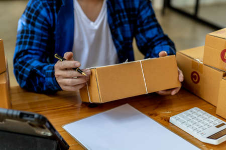 Asian person writing customer's shipping information on parcel box, He owns an online store, He ships products to customers through a private courier company. Online selling concept.の写真素材