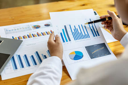 Businesswoman's hand holding a pen pointing at a bar chart on a corporate financial information...