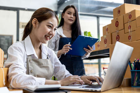 Two women are online sellers, concept online merchandising company, two female salespeople are answering customers and preparing packages according to orders that customers order through the website.の写真素材