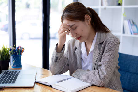 An Asian woman is tired of studying online on her laptop for a long time, she is a student. The concept of online learning due to the COVID-19 outbreak to prevent an outbreak in the classroom.の写真素材