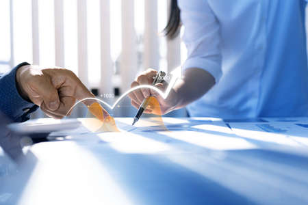 Two businessmen are meeting together, they point to financial documents to discuss plans and...