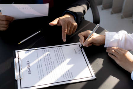 The home insurance salesman and the customer are signing an insurance agreement with their insurance company, accepting the terms and benefits. Home and real estate insurance concept.の写真素材
