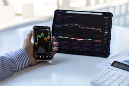 An investor is looking at stock charts on mobile phones and tablets, he is a stock investor, he...