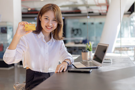 A woman sitting at the counter holding a credit card, she is shopping online and paying for goods...