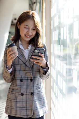 A woman playing a mobile phone by the window, a young businesswoman and a young executive founded a...